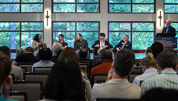 a woman speaking on a stage with an audience of 5 fellow speakers