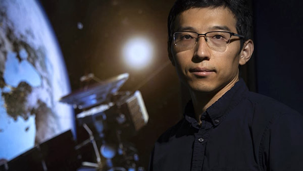 Xiao Huang in front of image of Earth and satellite 
